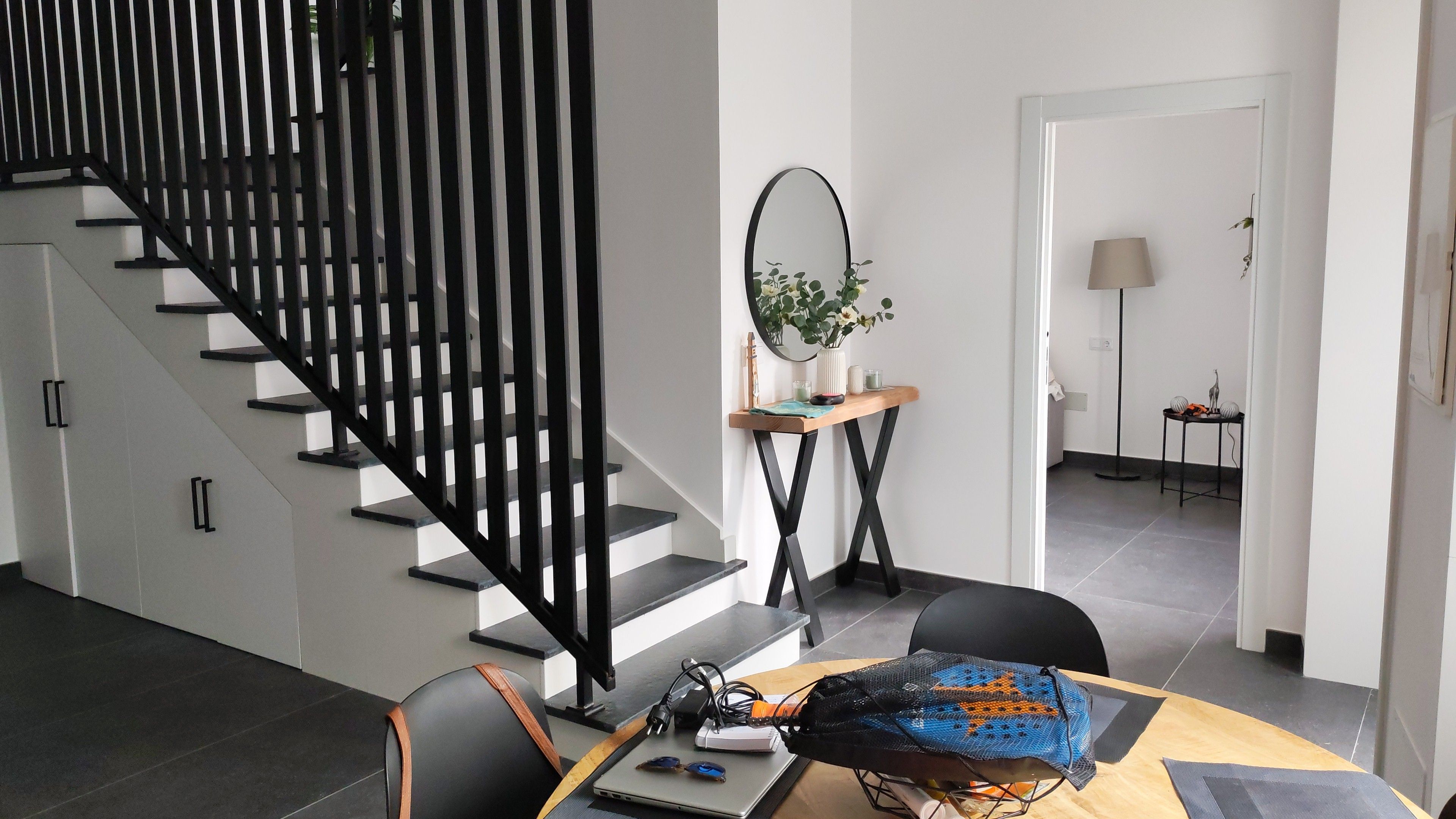 A modern interior with a staircase, a desk with a laptop, and a dining area.