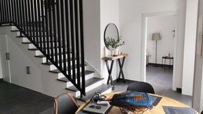 A modern interior with a staircase, a desk with a laptop, and a dining area.
