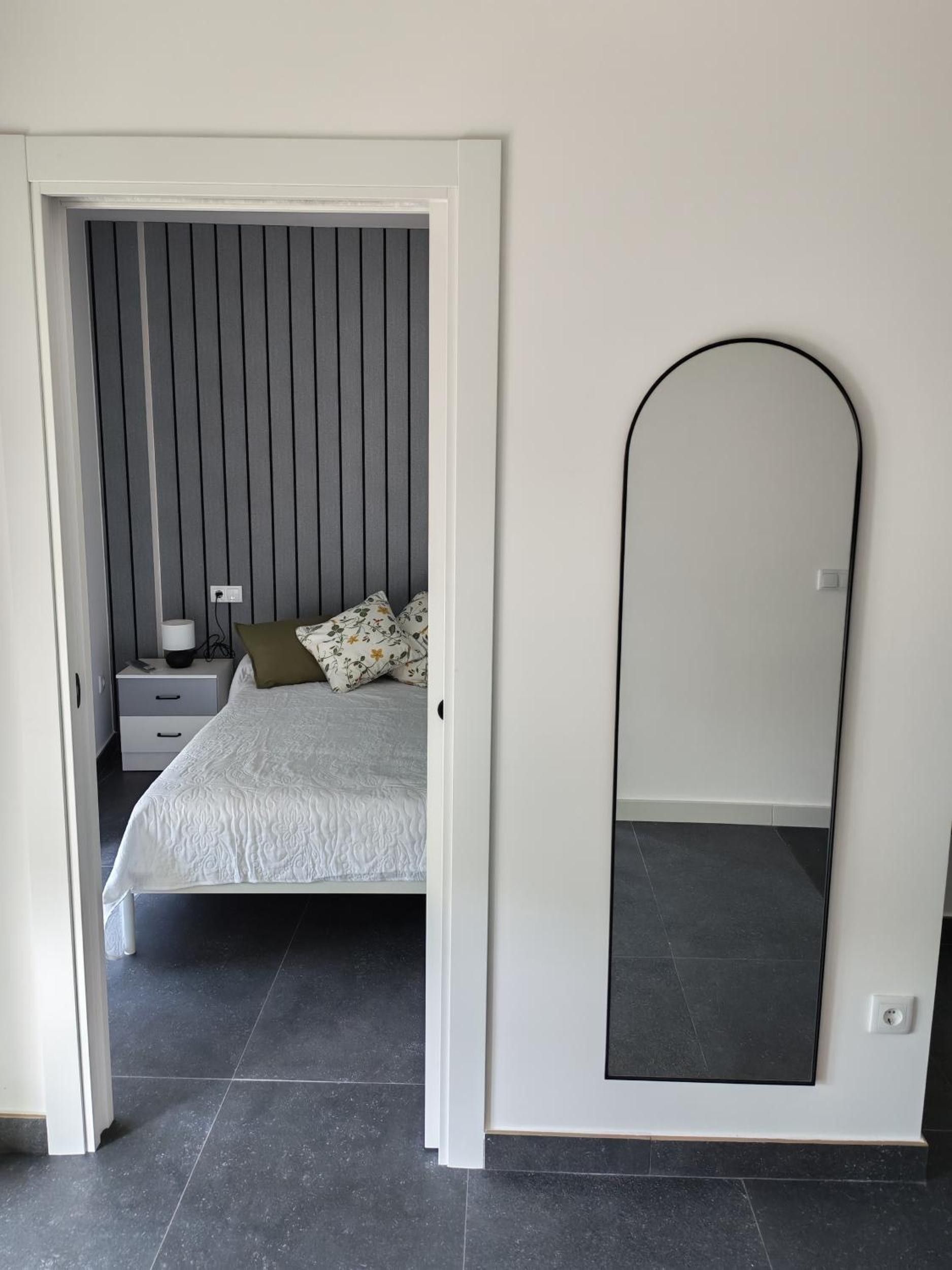 A bedroom with a bed, a nightstand, a lamp, and a mirror.