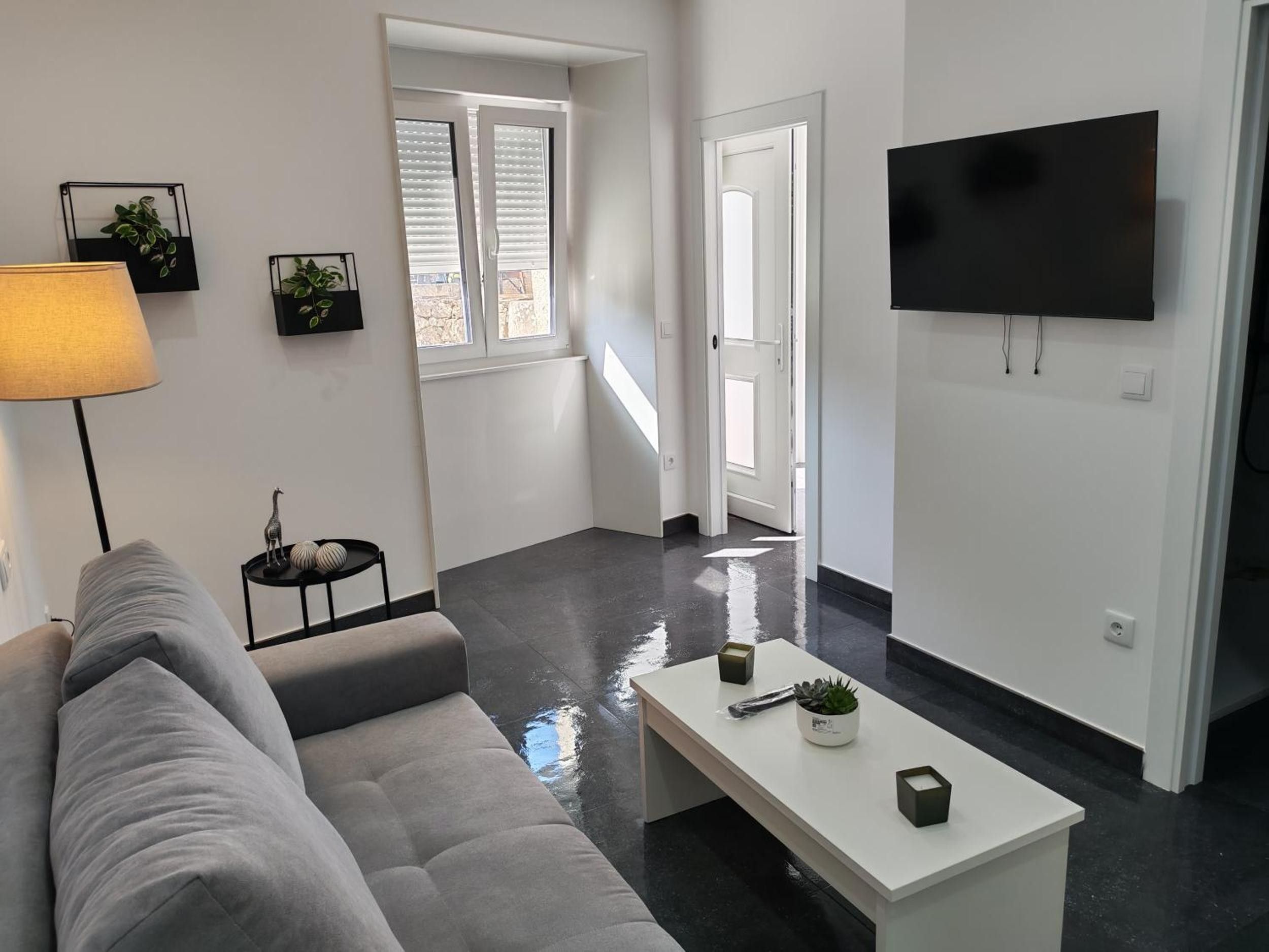 A modern living room with a grey sofa, a white coffee table, and a flat-screen TV mounted on the wall.