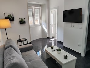 Una sala de estar moderna con un sofá gris, una mesa de centro blanca y un televisor de pantalla plana montado en la pared.
