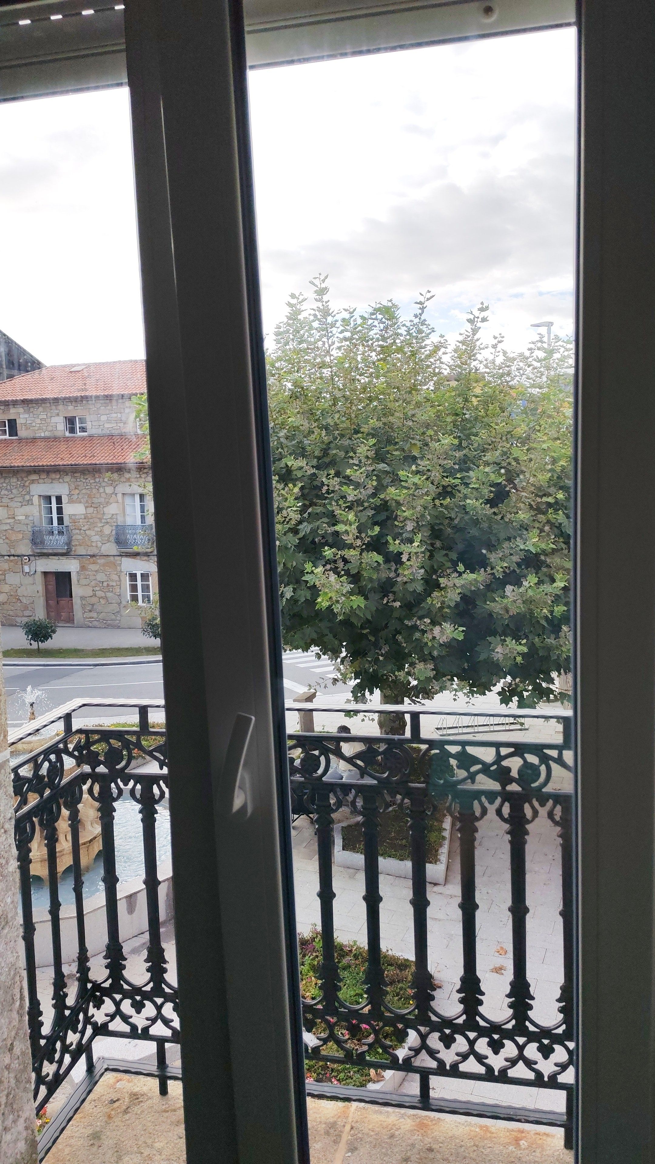 Vista desde un balcón con un edificio de piedra y un árbol al fondo.