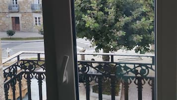 Vista desde un balcón con un edificio de piedra y un árbol al fondo.