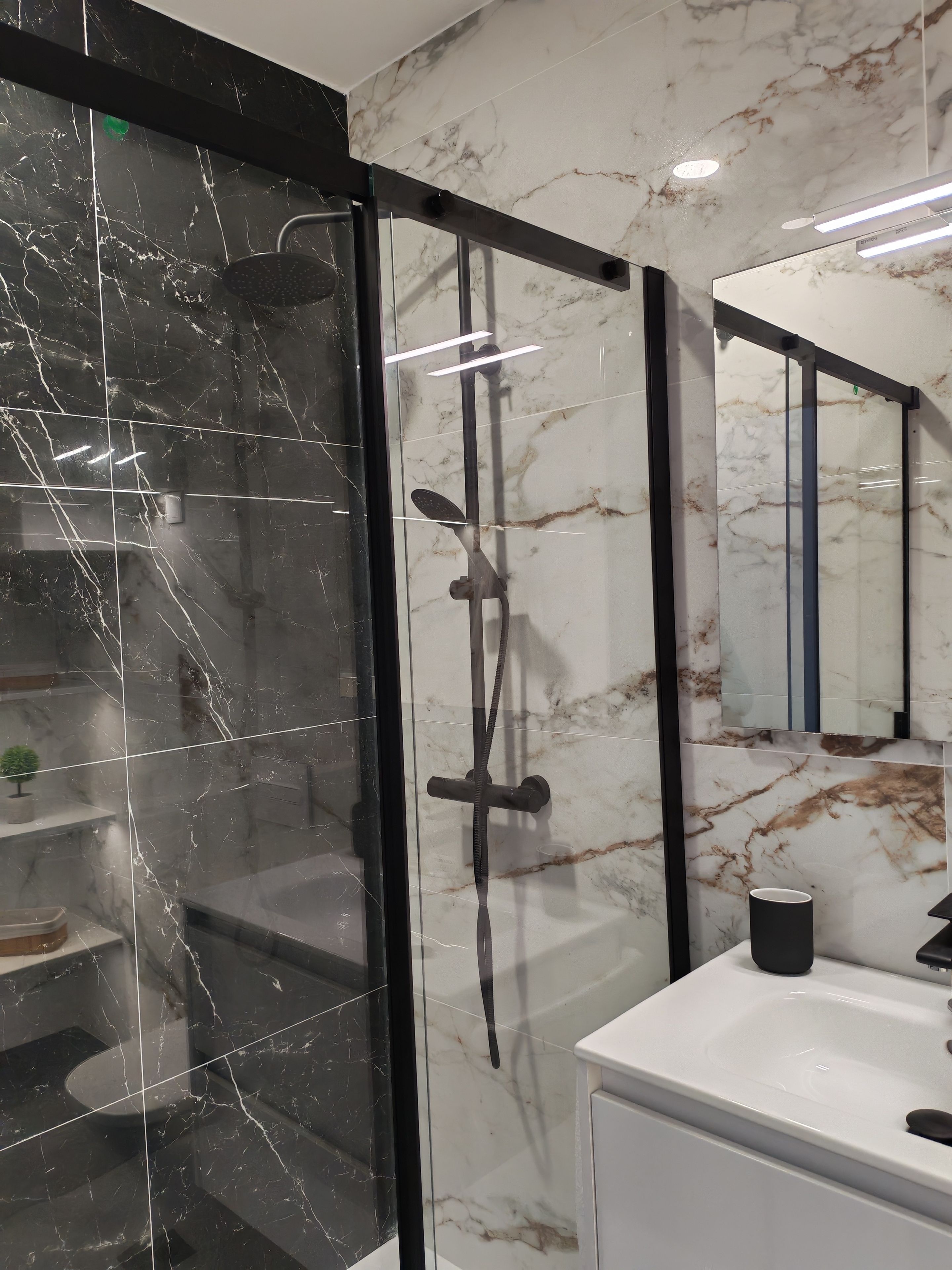 Un baño moderno con ducha envuelta en cristal, un lavamanos blanco y pared revestida de mármol.