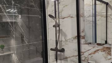 Un baño moderno con ducha envuelta en cristal, un lavamanos blanco y pared revestida de mármol.