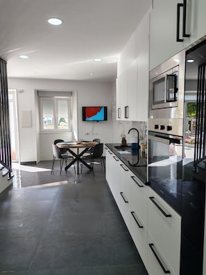 Una cocina moderna con comedor, muebles blancos, electrodomésticos de acero inoxidable y un televisor de pantalla plana montado en la pared.