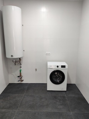 Pequeña lavandería con un calentador blanco de pared y una lavadora de carga frontal.