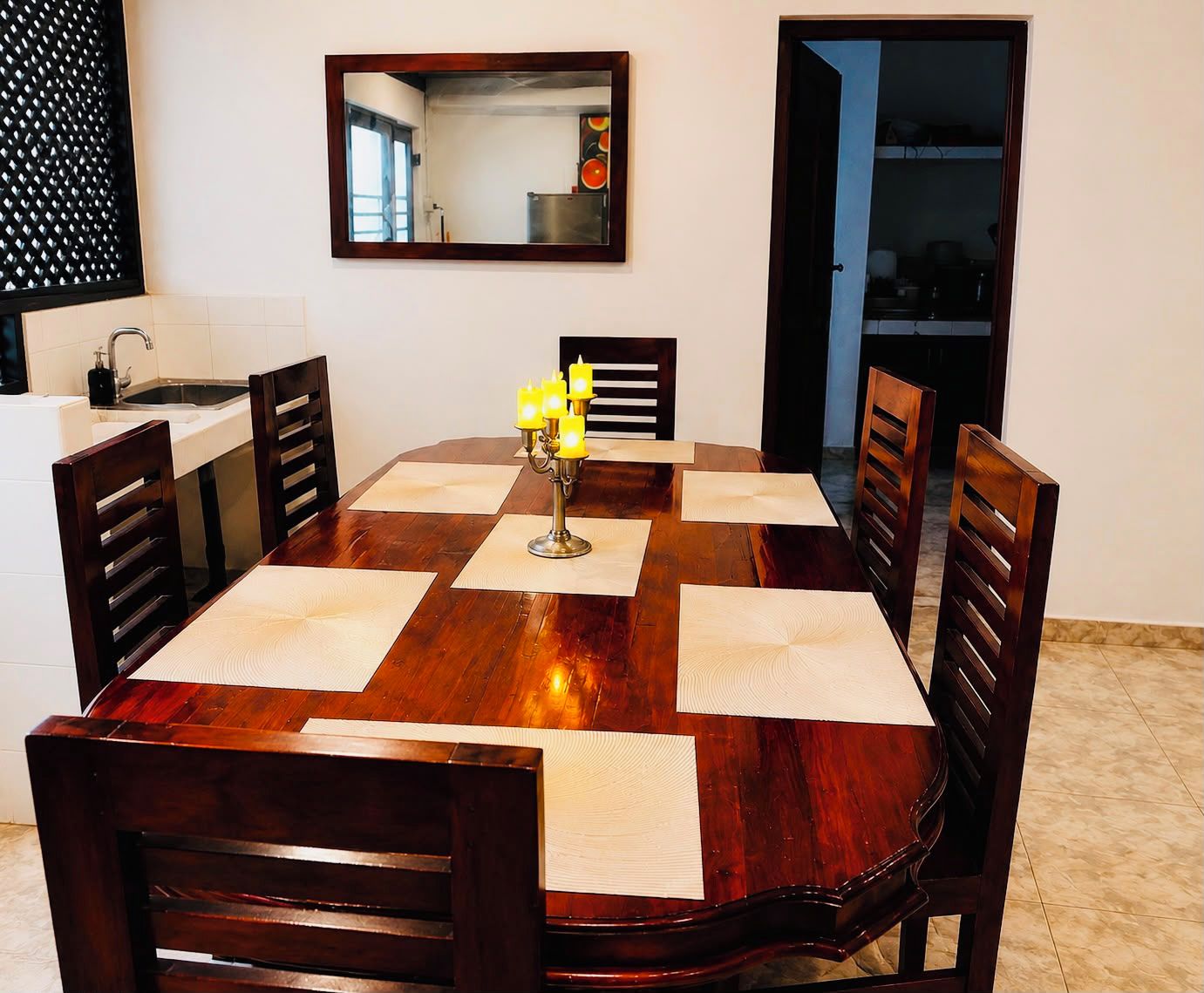 A dining table with six chairs, a candelabra with candles, and a mirror on the wall.