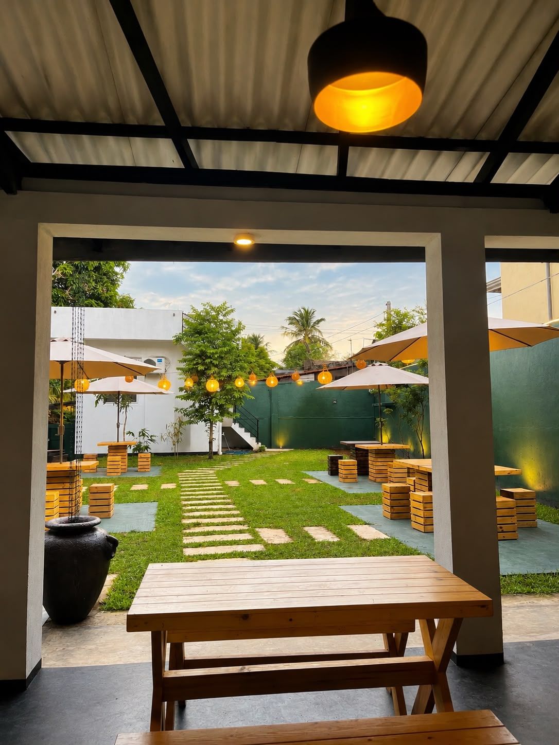 Eine Terrasse im Freien mit Holztischen und -bänken, einer Rasenfläche und Sonnenschirmen.
