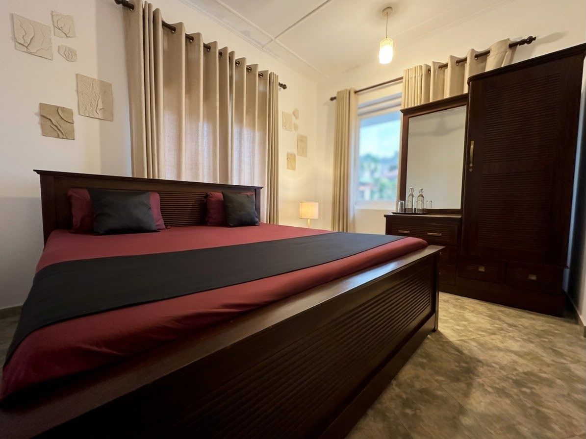 Ein Hotelzimmer mit einem großen Bett, einem Schminktisch, einem Spiegel und einem Fenster mit Vorhängen.