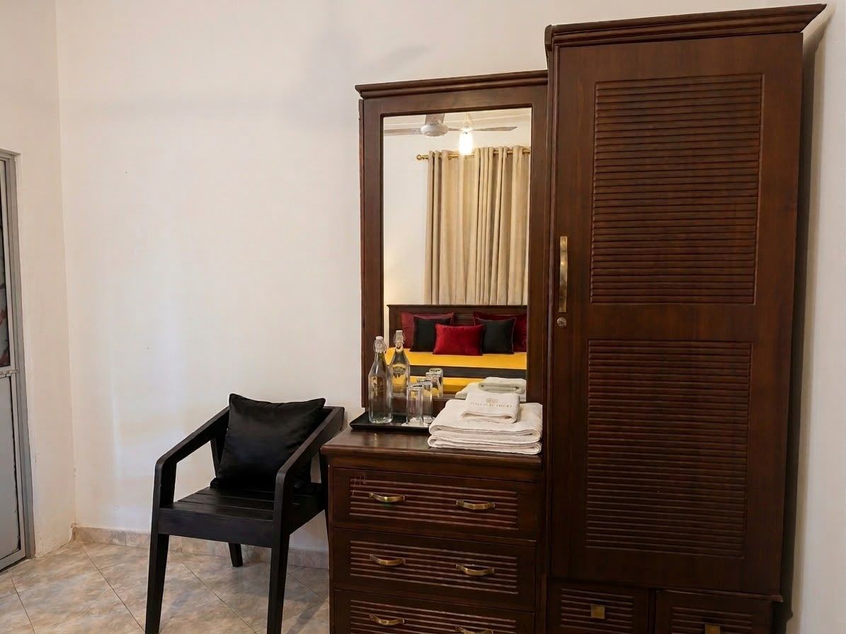 A wooden wardrobe with a mirror, a small black chair, and a tray with toiletries.