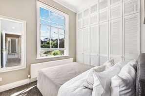 A bedroom with a large window, a bed with white bedding, and a white wardrobe. - Lovely large one bedroom flat with a balcony (London)
