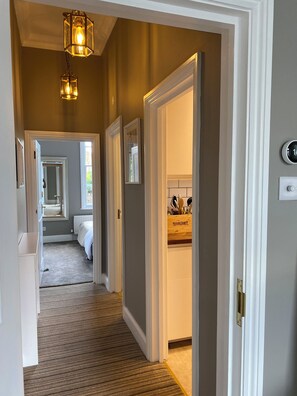 A hallway with a carpeted floor, a door leading to a bathroom, and a light fixture above. - Lovely large one bedroom flat with a balcony (London)