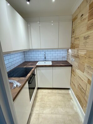 Een keuken met witte kastjes, een zwart inductiekookplaatje, een witte spoelbak en een houten achterwand.