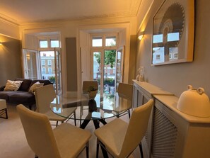 A modern living room with a glass table, comfortable seating, a sofa, and a fireplace. - Lovely large one bedroom flat with a balcony (London)