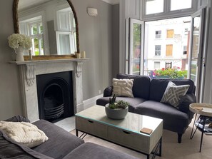 A living room with a fireplace, a sofa, a coffee table, and a view of the outside. - Lovely large one bedroom flat with a balcony (London)