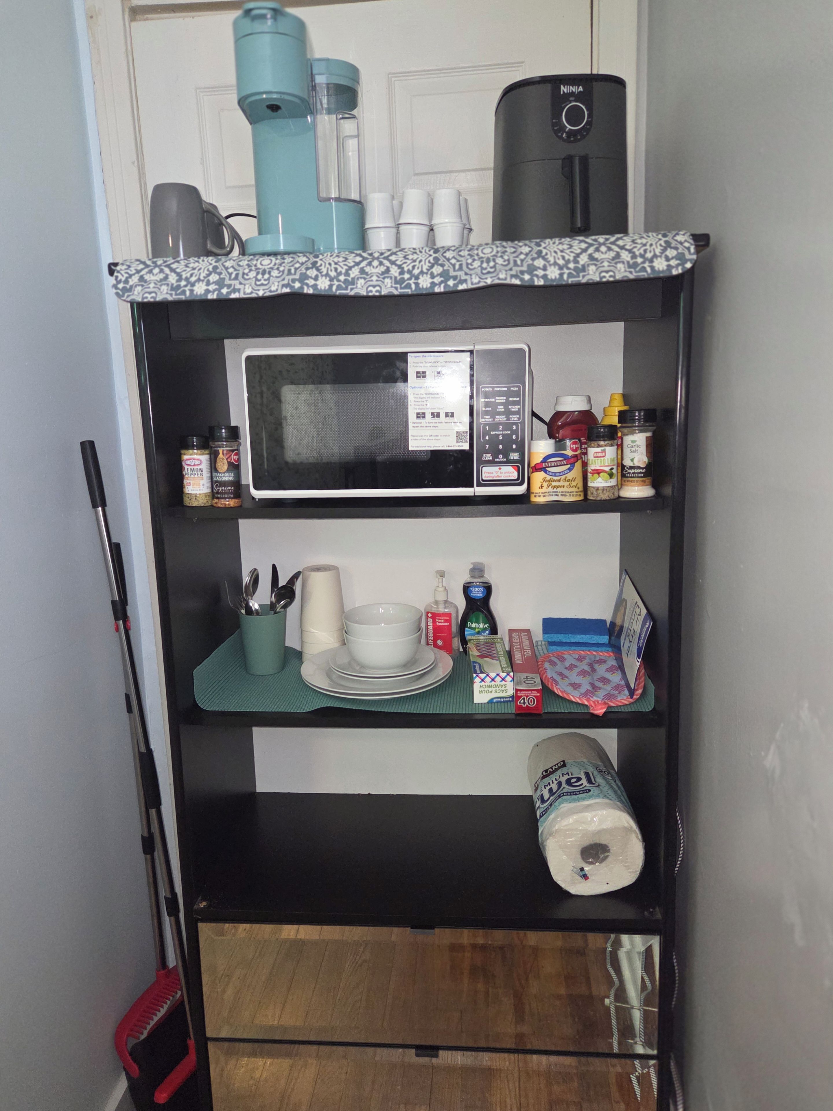 A kitchen shelf with a microwave, various kitchen utensils, a roll of paper towels, and a coffee maker.
