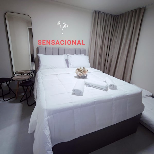 A hotel room with a bed, a small table with chairs, a mirror, and a window with curtains. - Sensational Apartment Liberdade SP (São Paulo)