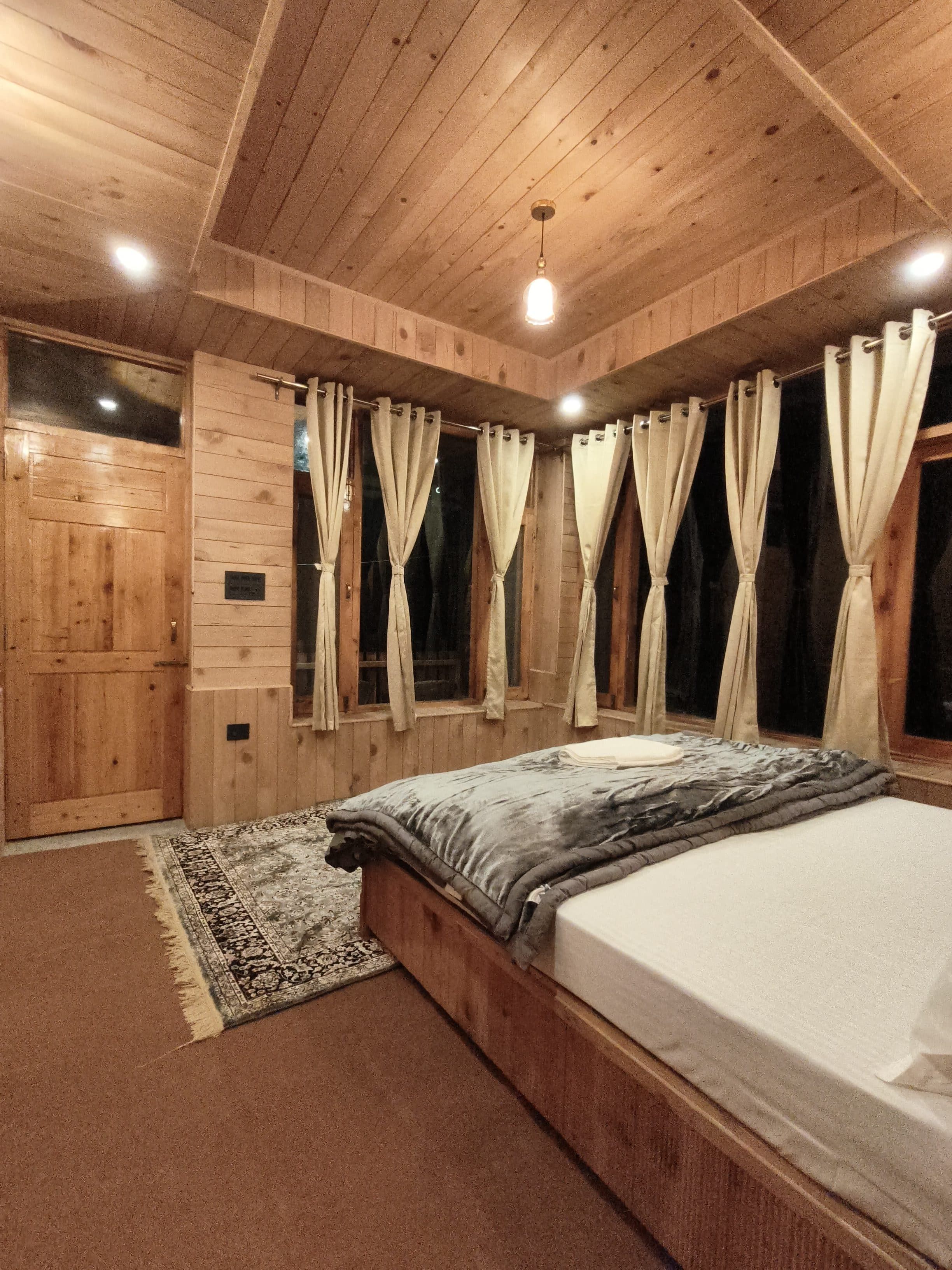 A wooden-paneled room with a bed, curtains, and a rug.