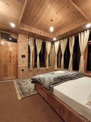 A wooden-paneled room with a bed, curtains, and a rug. - The Tirthan Valley Wooden House  (Banjar)