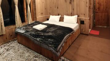 Une pièce aux murs lambrissés, avec un lit, des rideaux, un tapis et une porte.