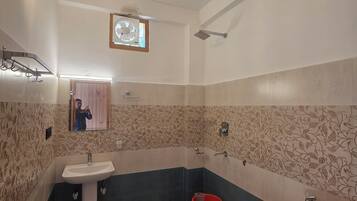 Une salle de bain avec un lavabo, un miroir, une douche et un seau rouge.