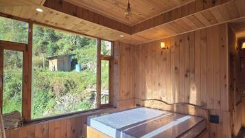 Un intérieur en bois avec un lit, de grandes fenêtres et une vue sur la verdure environnante.