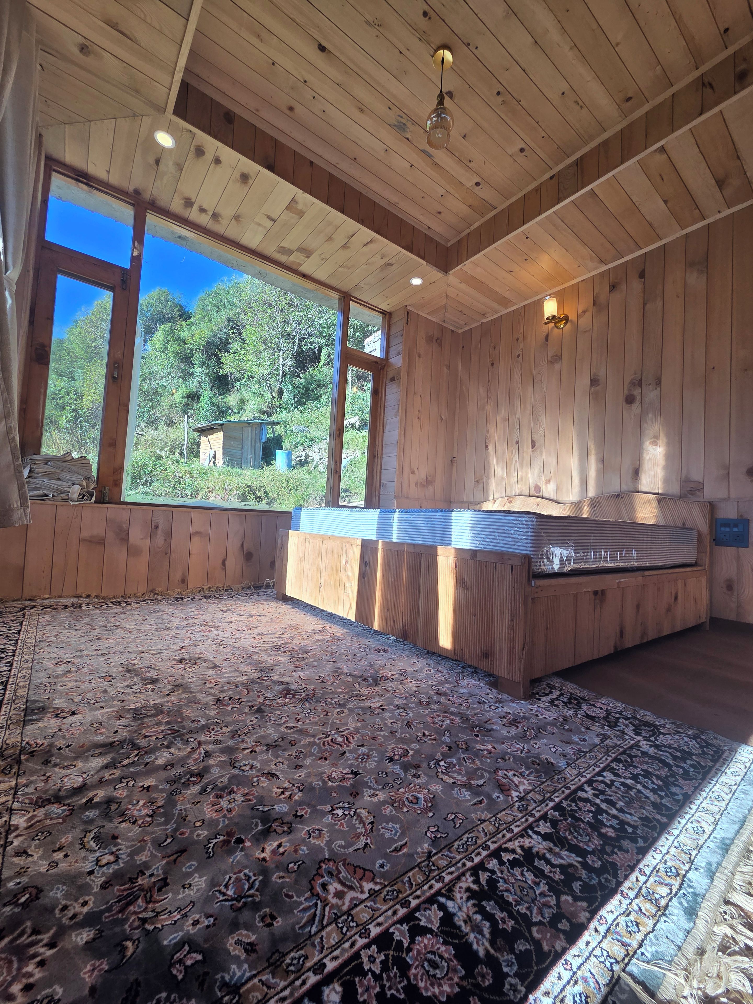 Ein Zimmer mit einem großen Fenster, einer Holzbalkendecke und einem gemusterten Teppich.