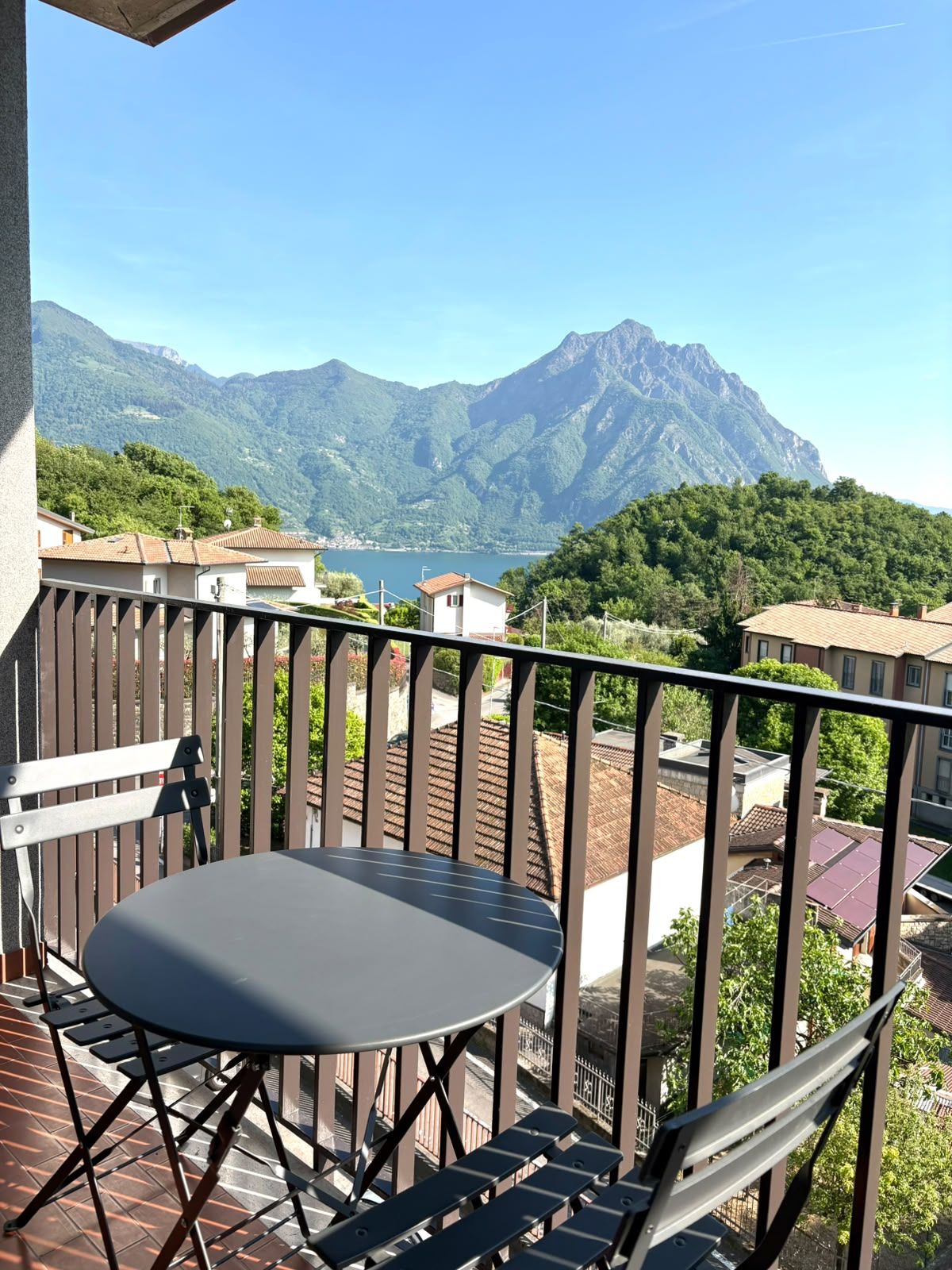Een balkon met een tafel en stoelen, met uitzicht op een bergachtig landschap en een wateroppervlak.
