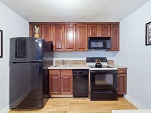 A kitchen with wooden cabinets, a black refrigerator, a microwave, a stove, and a dishwasher. - Delightful 1-bedroom condo in vibrant Denver perfect for your stay (Denver)