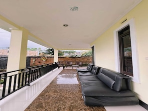 A covered balcony with a marble floor, a black leather sofa, and a small table. - Cozzy Villa HN (Cisarua)