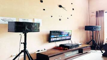 A room with a wall clock, a television on a stand, and two speakers on stands.