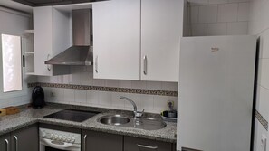 A kitchen with white cabinets, a stainless steel sink, a built-in oven, and a refrigerator. - Jédula Apartment (Jédula)