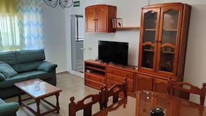 Een woonkamer met een bank, televisie, houten kast en eettafel.