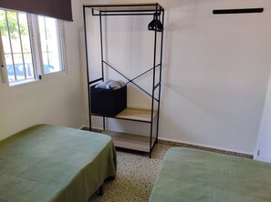 Een kamer met twee bedden, een metalen kledingkast en een raam.