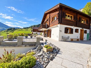 Eine Holzchalet mit Balkon, Steintreppe und einem Gartenbereich mit Pflanzen und Steinen.