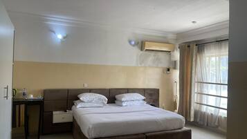 Een hotelkamer met een groot bed, een nachtkastje, een airconditioning en een raam met gordijnen.
