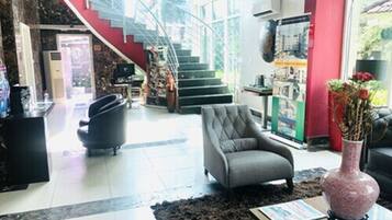 A modern lobby with a staircase, a grey armchair, a black sofa, a decorative vase, and a magazine on a table.