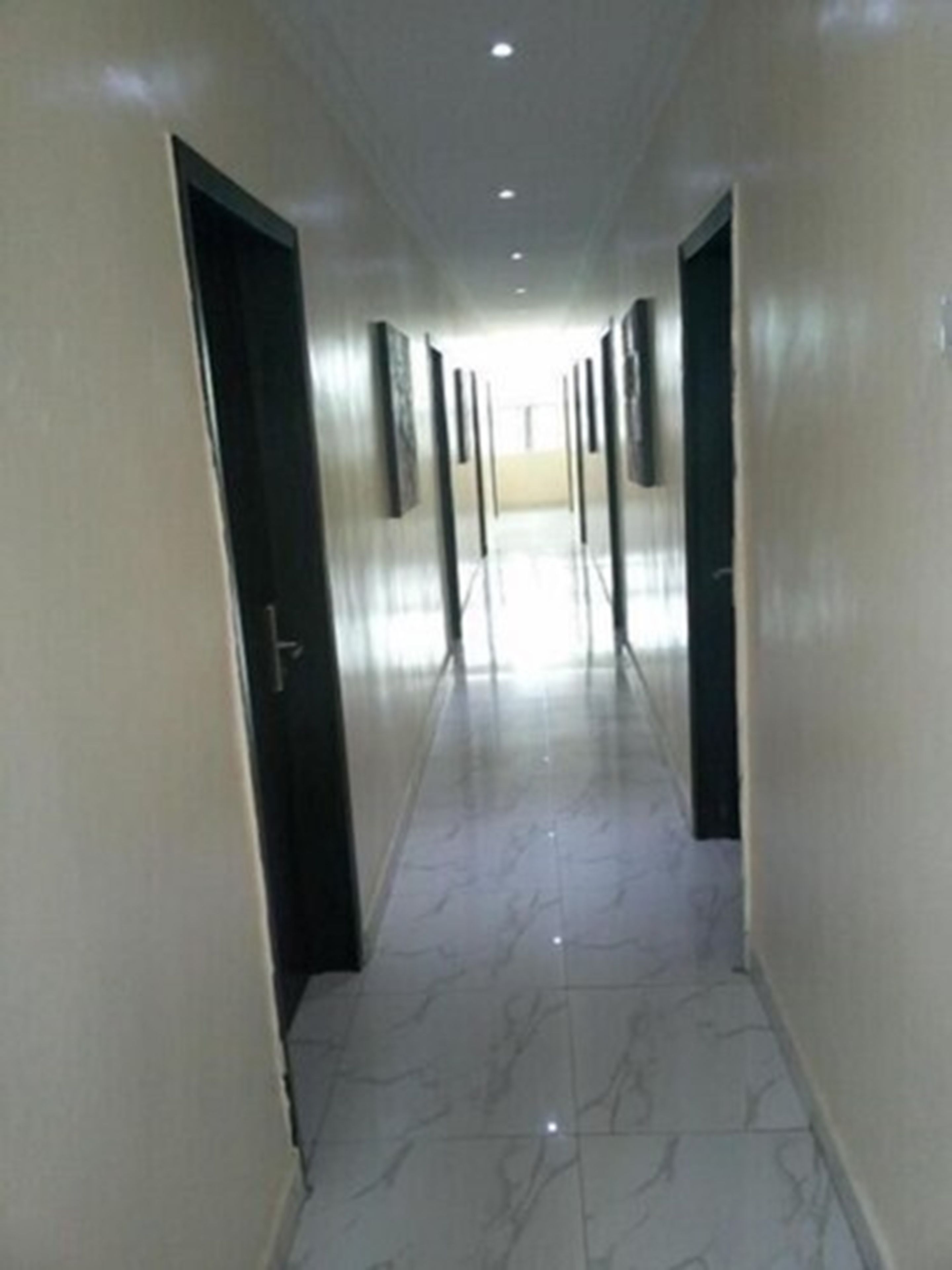 A corridor with doors on both sides, leading to a bright room at the end.