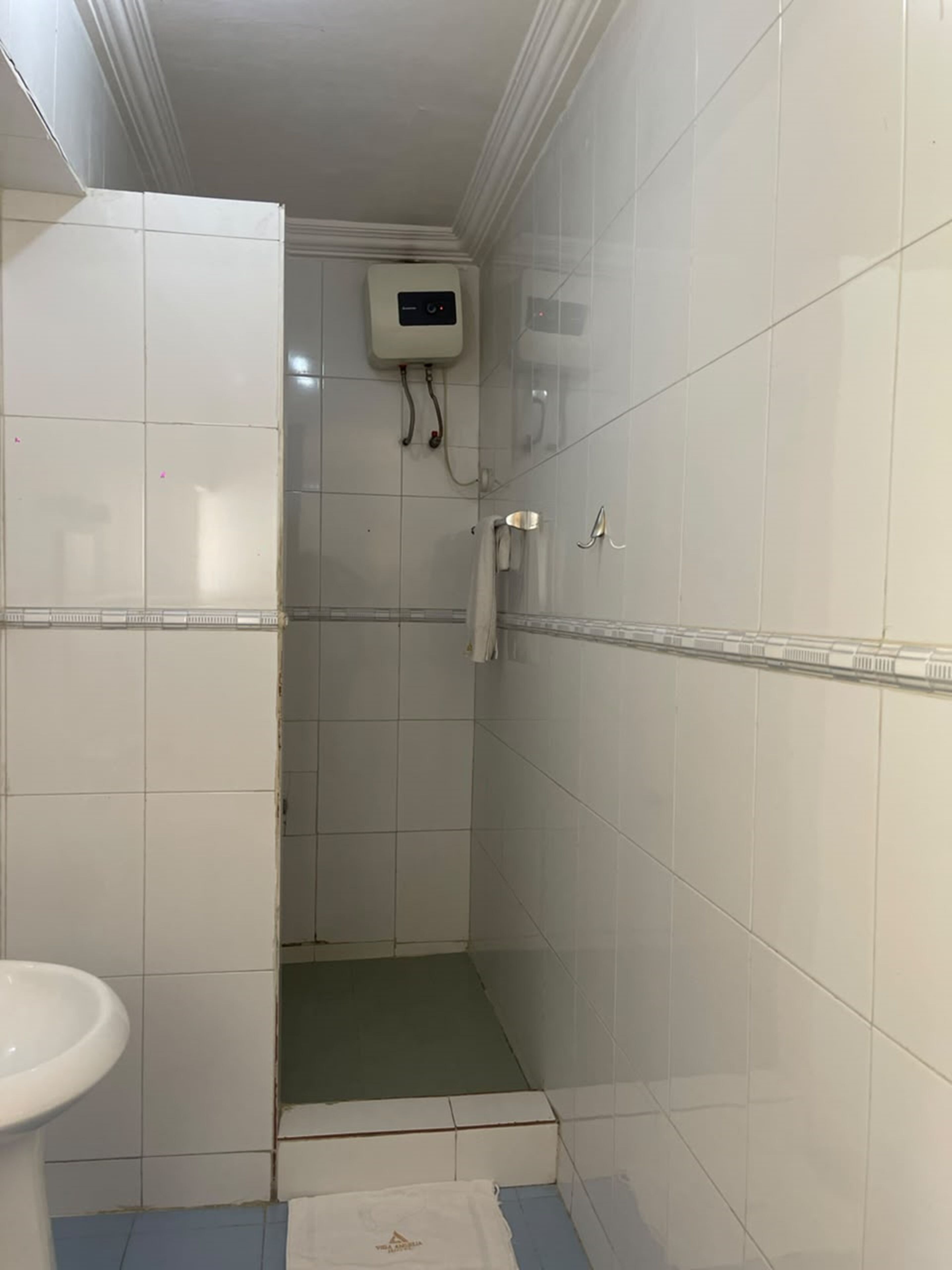 A small bathroom with white tiles, a toilet, a shower area, and a towel rack.