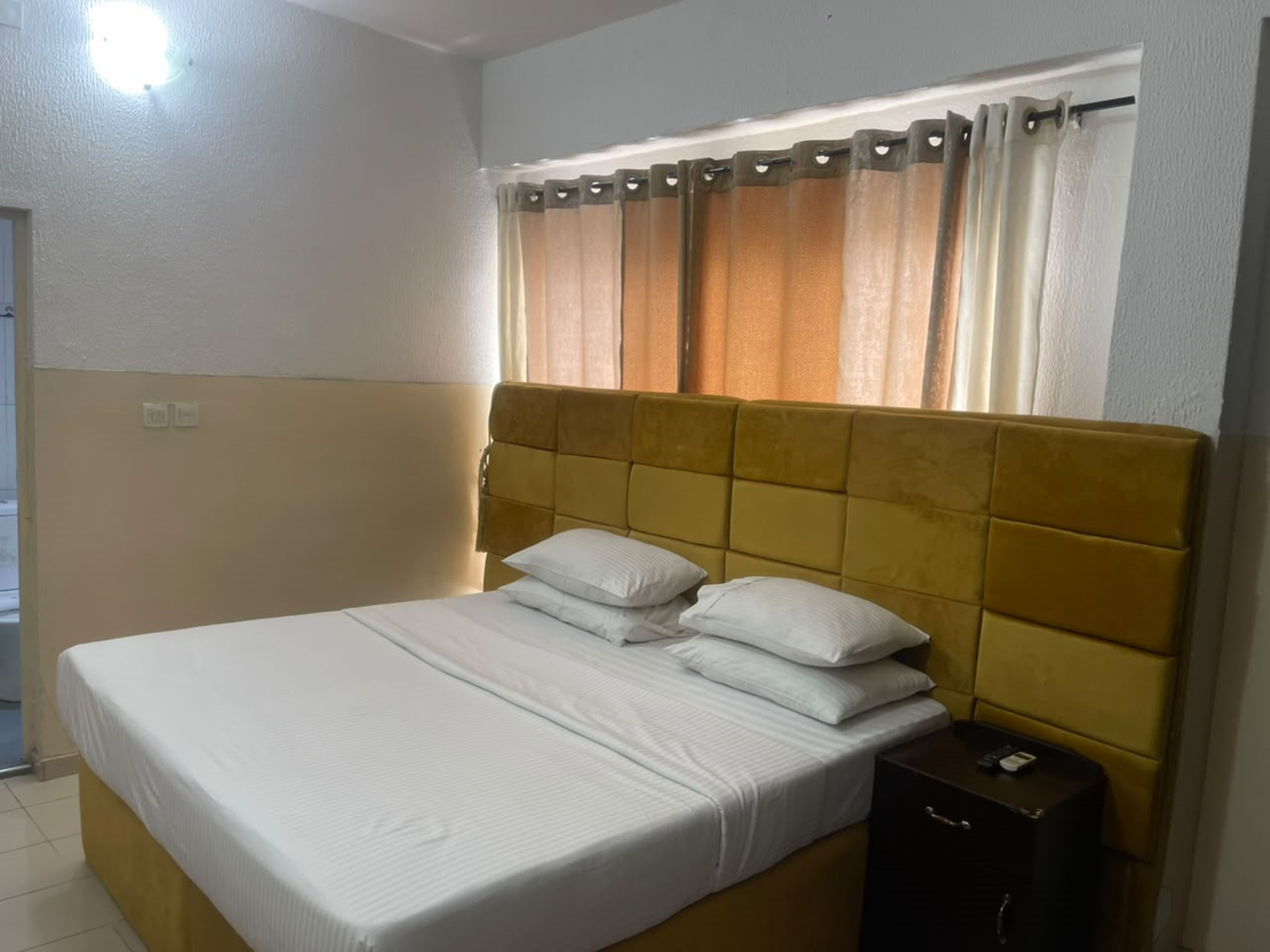 Habitación de hotel con cama, mesita de noche y ventana con cortinas.