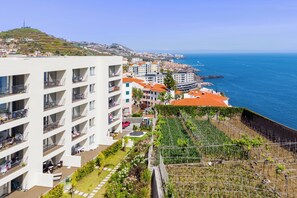 A coastal hotel with multiple balconies, a garden area, and a view of the sea. - Modern Seaview Apt with pool, 15 min Walk to Beach (Câmara de Lobos)