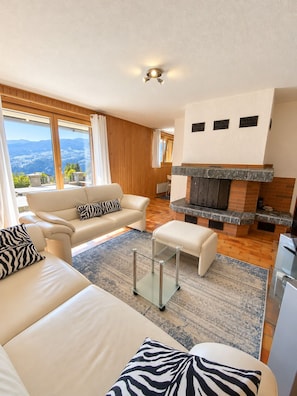 A modern living room with a fireplace, a sofa set, and a view of the outdoors. - Brienz Mountain Base – Simple & Comfortable (Brienz/Brinzauls)