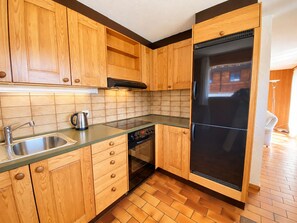 A kitchen with wooden cabinets, a stainless steel sink, a black refrigerator, and a tiled backsplash. - Brienz Mountain Base – Simple & Comfortable (Brienz/Brinzauls)