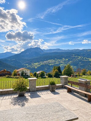 A scenic outdoor seating area with stone benches and planters, overlooking a mountainous landscape with houses and greenery. - Brienz Mountain Base – Simple & Comfortable (Brienz/Brinzauls)