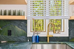 A kitchen with a stainless steel sink, a gold faucet, and a window with blinds. - Saugatuck Escape | Hot Tub • Walkable • Designer! (Saugatuck)