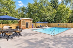 Ein Swimmingpool mit Liegestühlen und Sonnenschirmen, umgeben von einem Holzzaun und Bäumen.