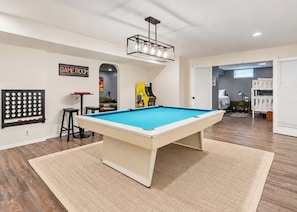 A pool table in a room with a 'GAME ROOM' sign, a pinball machine, and a billiards rack. - Blue Haven Retreat | Pool • Theater • Arcade Room! (Fennville)