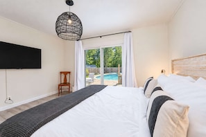 A bedroom with a large bed, a television, and a view of a swimming pool. - Blue Haven Retreat | Pool • Theater • Arcade Room! (Fennville)