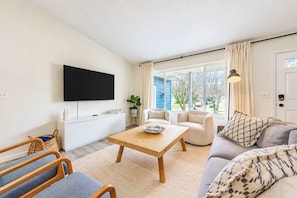 A living room with a flat-screen TV, a wooden coffee table, a sofa, and a chair. - Blue Haven Retreat | Pool • Theater • Arcade Room! (Fennville)